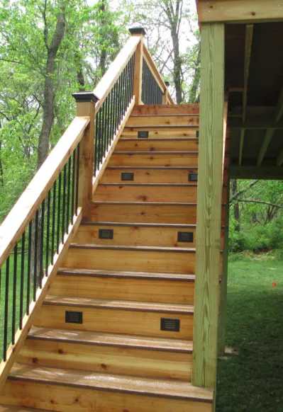 Custom cedar deck staircase with integrated step lighting built by Pro Deck & Design in Kansas City, featuring black metal balusters, premium wood construction, and professional installation for safe access in wooded Leavenworth County properties