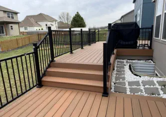 Modern composite deck with black aluminum railings installed by Pro Deck & Design in Kansas City, featuring integrated stairs, decorative stone border, and custom grilling station perfect for outdoor entertaining in new Wyandotte County subdivisions